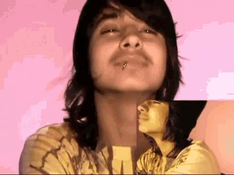 a young man with a mustache and a piercing in his lip is looking at the camera .