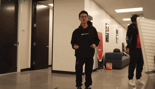 a man wearing a black hoodie that says infinity walks through a hallway