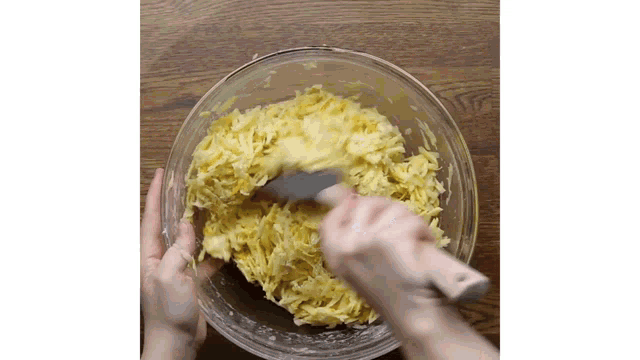 a person is mixing a casserole in a bowl with a spatula .