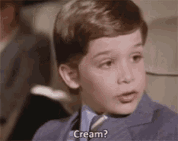 a young boy in a suit and tie is sitting in a chair and talking about cream .