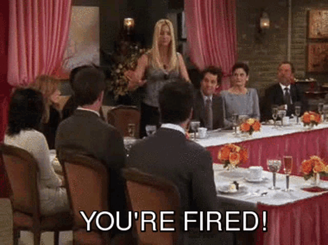 a group of people sitting at a long table with the words you 're fired on the bottom