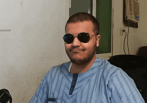 a man wearing sunglasses and a blue shirt smiles for the camera
