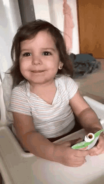 a little girl is sitting in a high chair holding a carton of juice .