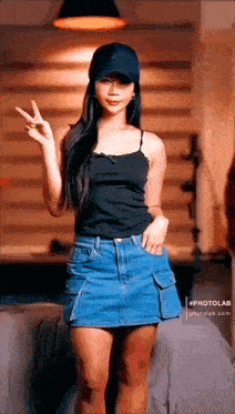 a woman wearing a black tank top and a denim skirt is making a peace sign .