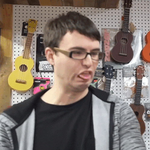 a man wearing glasses is making a face in front of a wall of guitars