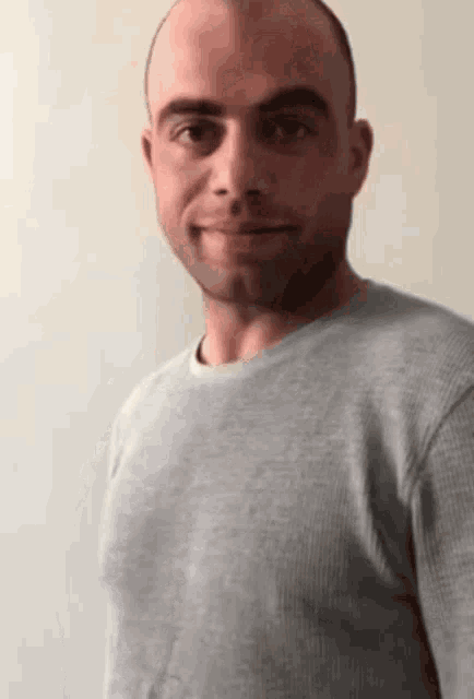 a man with a shaved head is wearing a gray sweater and smiling .