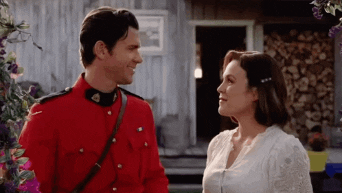 a man in a red uniform and a woman in a white dress are standing next to each other and looking at each other .