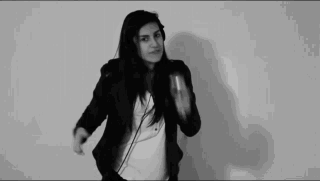 a woman in a black jacket and white shirt is dancing in a black and white photo