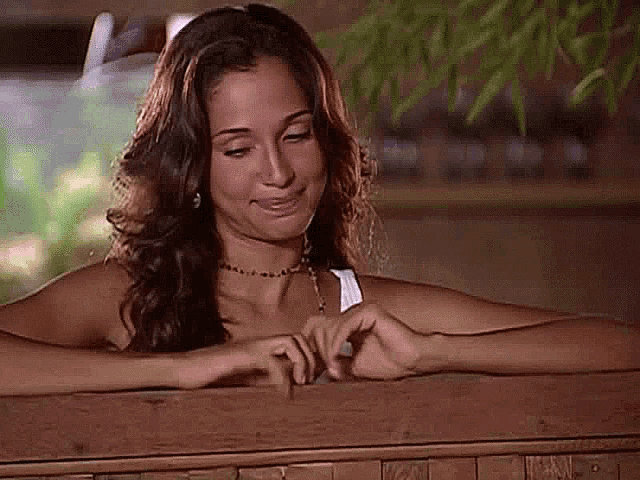 a woman is sitting on a wooden bench with her hands on the fence .