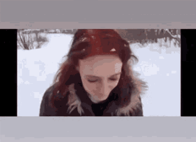 a woman with red hair is standing in the snow and looking at the camera .