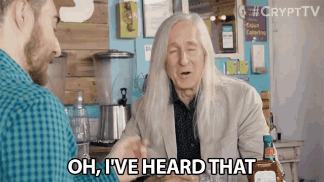 a man with long hair says oh i 've heard that while sitting at a table