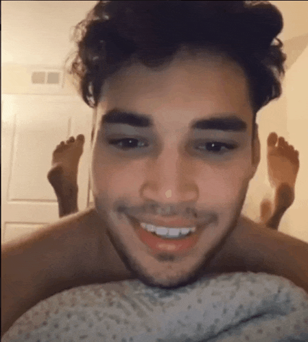 a man is smiling while laying on a bed with his feet up