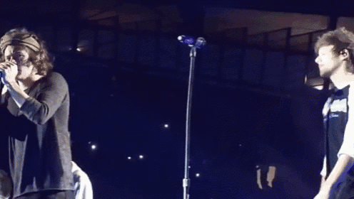 a man is singing into a microphone while another man stands behind him .