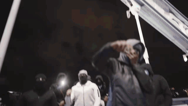 a group of men wearing face masks and hoodies are standing in a line .