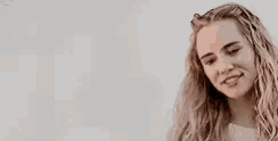 a woman with long blonde hair is smiling and looking down against a white background .