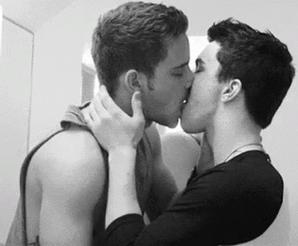 a couple of men are kissing in a black and white photo .