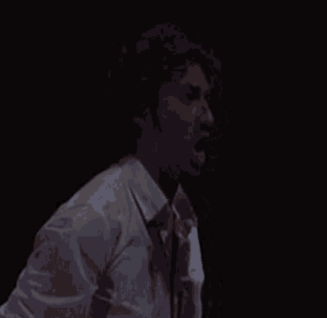 a man in a bloody shirt and tie is screaming into the air .