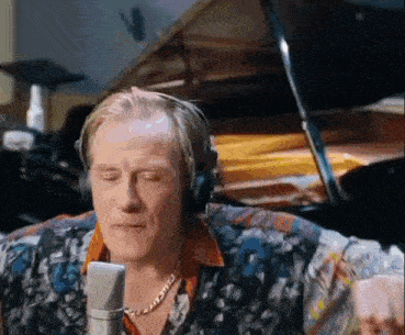 a man wearing headphones is singing into a microphone while sitting in front of a piano .