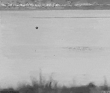 a black and white photo of a helicopter flying over a body of water