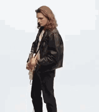 a young man in a leather jacket is playing a guitar .