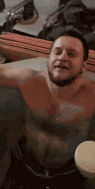 a shirtless man is sitting in a bathtub with his arms outstretched