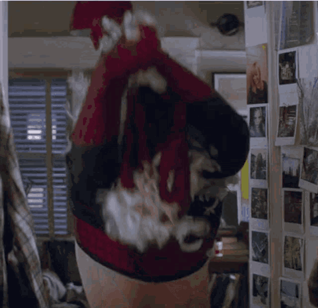 a man wearing a santa hat is standing in front of a wall of pictures .