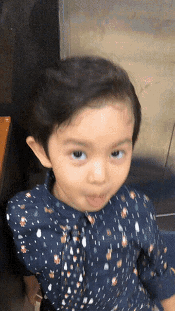 a little girl wearing a blue shirt with polka dots making a face