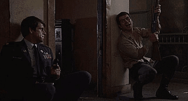 a man is holding a gun in a doorway while another man holds a gun in a room .