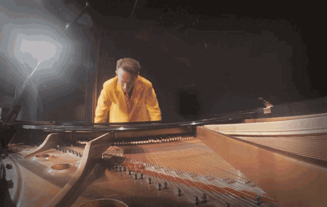 a man in a yellow jacket is looking at a piano