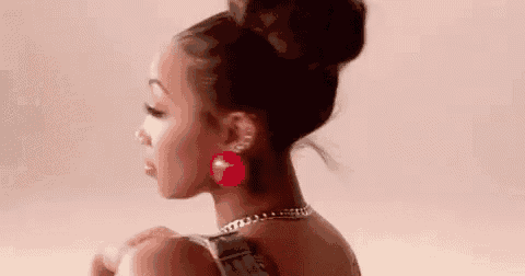 a woman with her hair in a bun and red earrings is wearing a necklace .