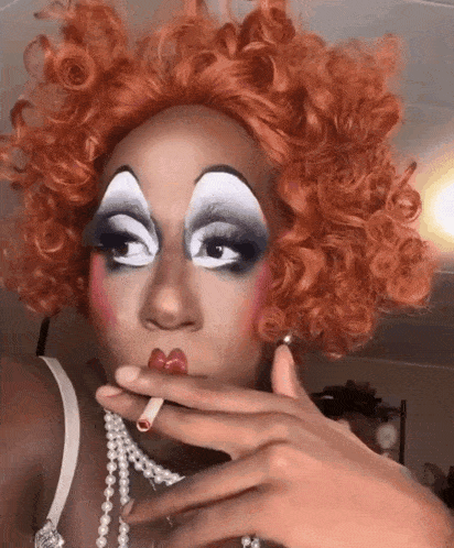 a drag queen is smoking a cigarette while wearing a pearl necklace