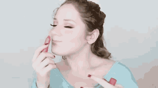 a woman is applying lipstick to her lips while wearing a blue shirt .
