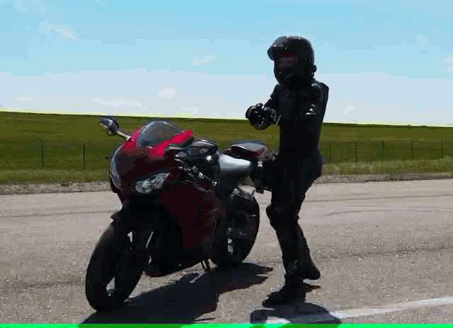 a man in a helmet stands next to a red motorcycle on the side of the road