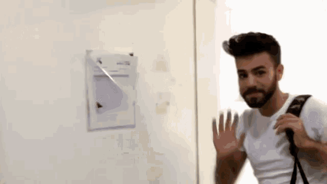 a man with a beard is standing in front of a white wall with a piece of paper on it