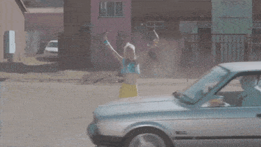 a woman in a blue shirt is sitting in a car with her arms outstretched