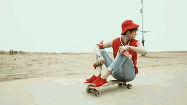 a man in a red hat sits on a skateboard on a beach