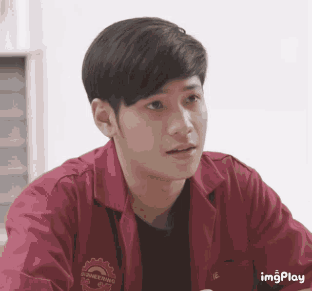 a young man wearing a red engineering shirt looks at the camera