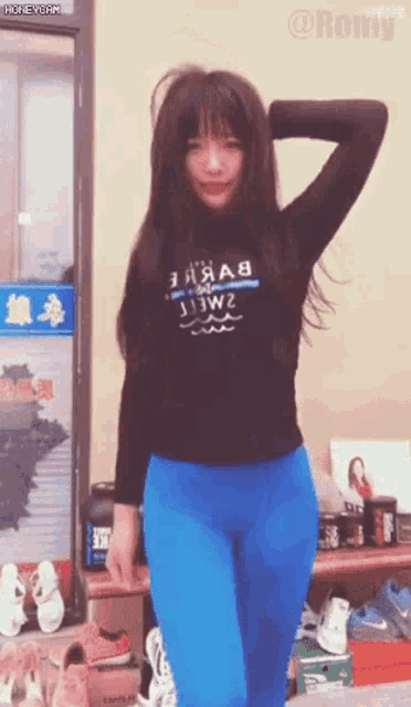 a woman wearing a black shirt and blue leggings is standing in front of a shoe rack .