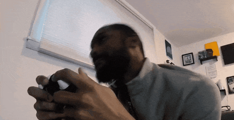 a man with a beard is holding a remote control in front of a window