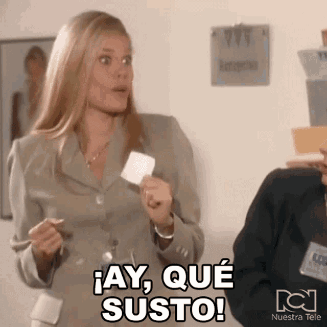 a woman in a suit is holding a piece of paper and says " ay que susto "