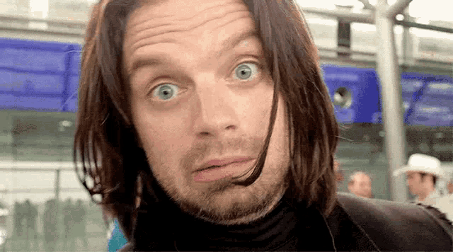 a man with long hair and a beard is making a funny face at the camera .