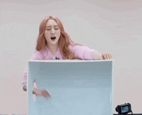 a woman in a pink sweater is screaming into a blue box