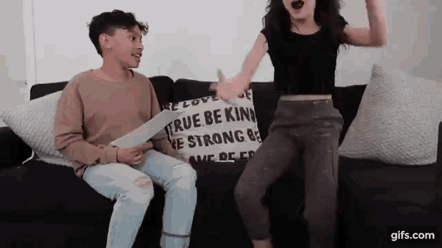 a boy and a girl are sitting on a couch with a pillow that says `` true be kind '' .