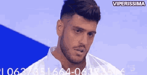 a man with a beard and a white shirt is looking at the camera with a blue background .
