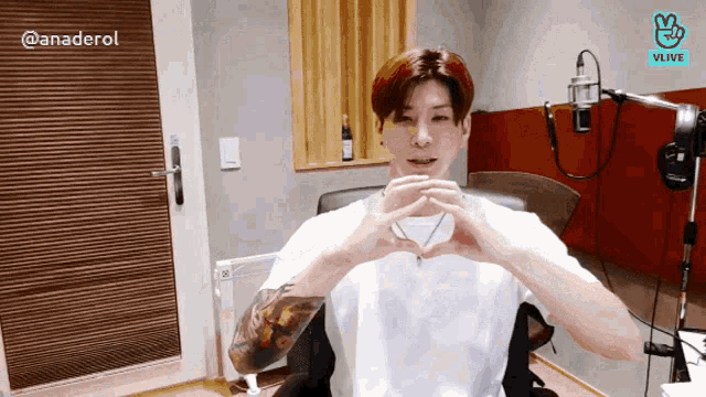 a man in a white shirt is making a heart shape with his hands in front of a microphone