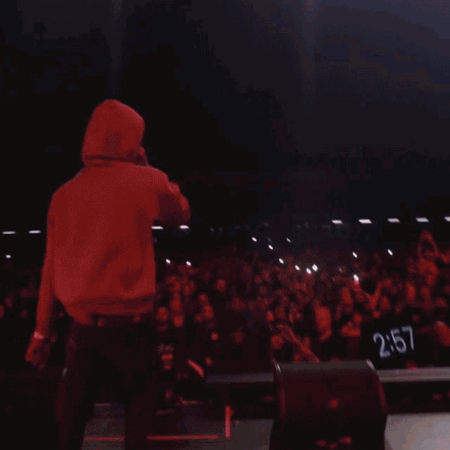 a man in a hoodie stands on a stage in front of a crowd with the number 230 on the wall