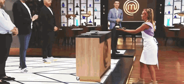 a woman in a white apron is standing in front of a table with a m on it