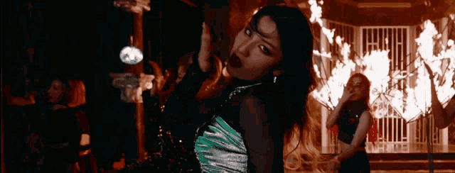 a woman in a green dress is standing in front of a fire in a dark room .