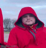 a man in a red jacket with a hood is holding a sword .