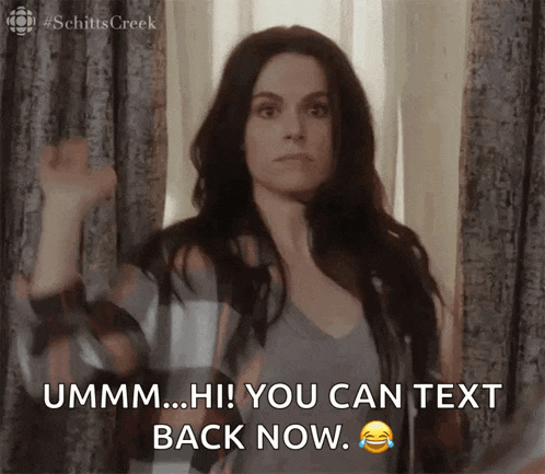 a woman is standing in front of a window and says " ummm hi ! you can text back now "